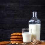 Glass of milk with stack of cookies, book, and bottle on a rustic wooden table.